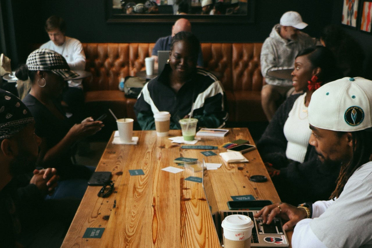People sitting around a wooden table in a bar setting with drinks and When We Commune cards.